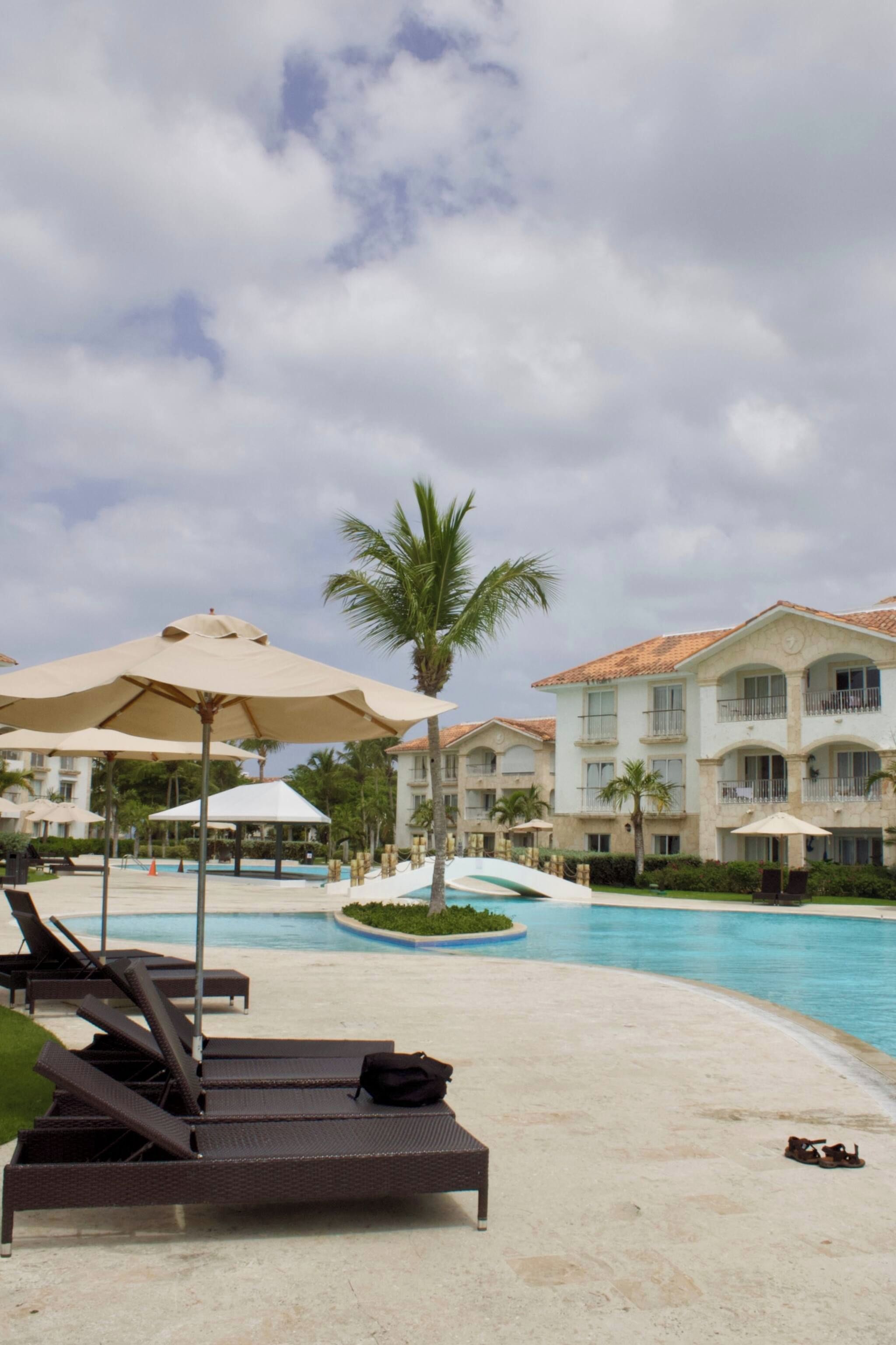 A resort pool area with lounge chairs and umbrellas, surrounded by a building with balconies.