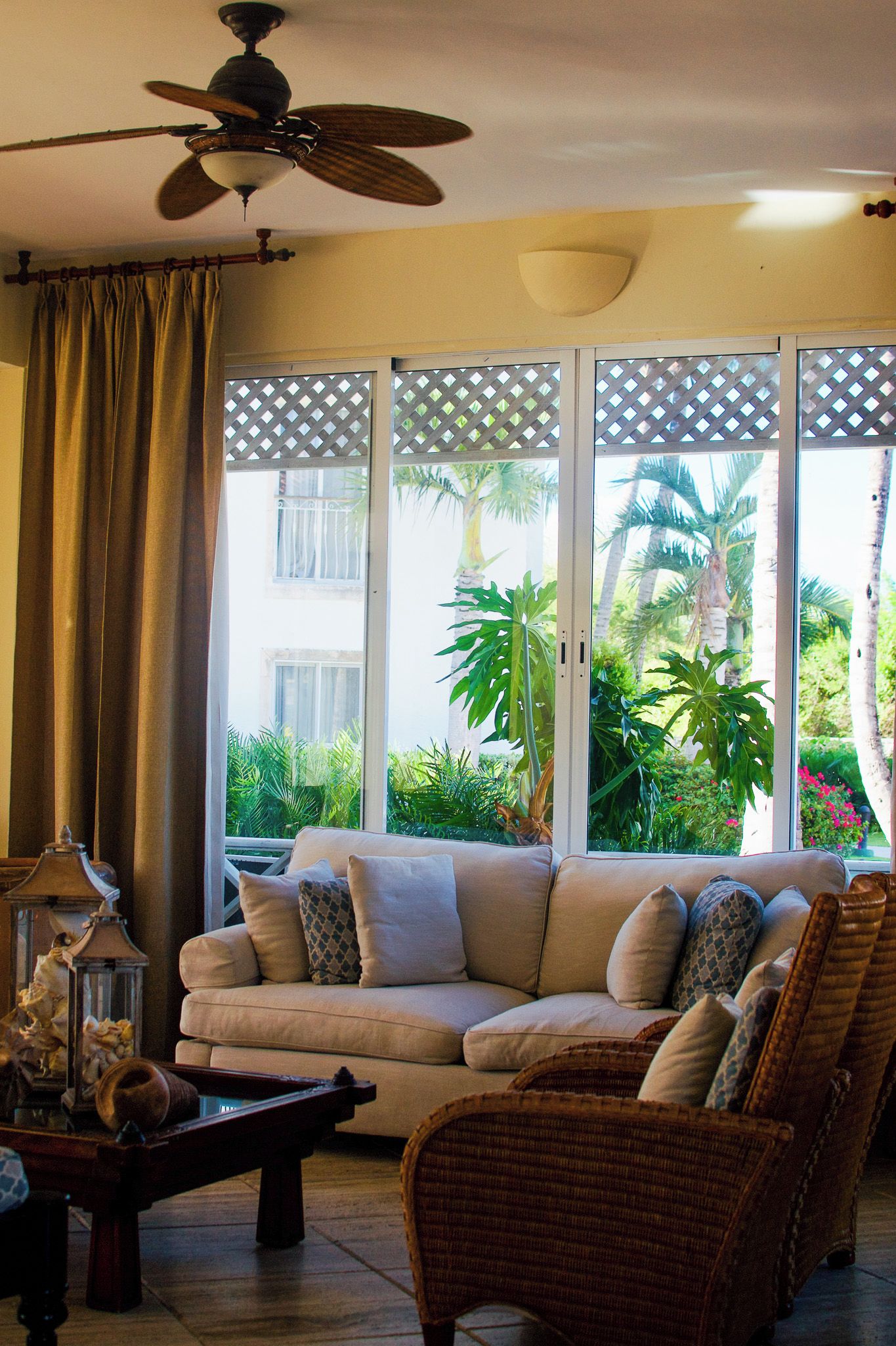A living room with a beige sofa, a wicker chair, a coffee table, and a ceiling fan.