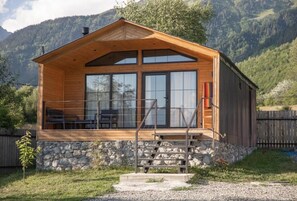 Una cabaña de madera con base de piedra, ventanas amplias y una escalera que conduce a un porche cubierto.