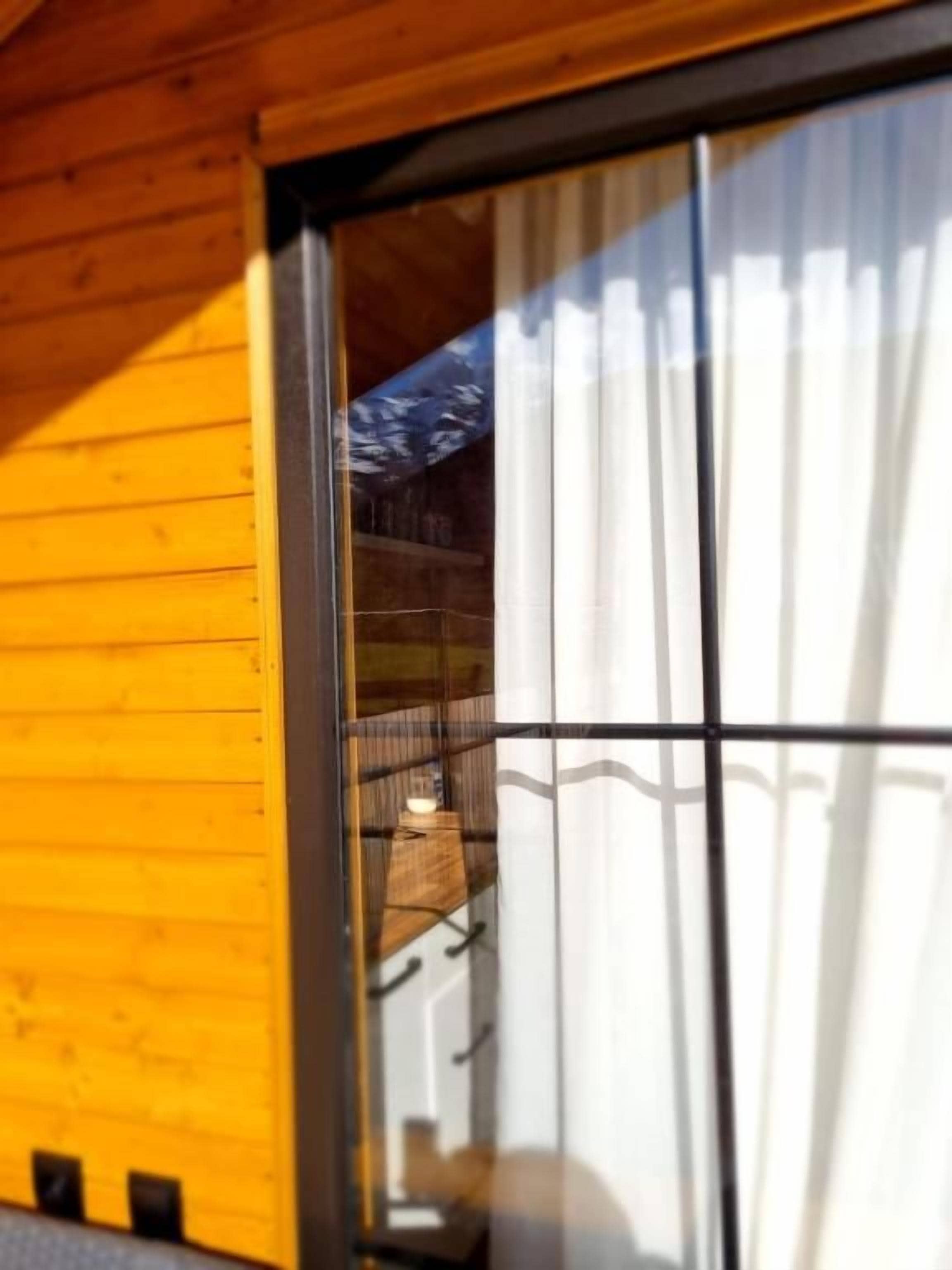 A wooden exterior wall with a window reflecting a building and a mountain.