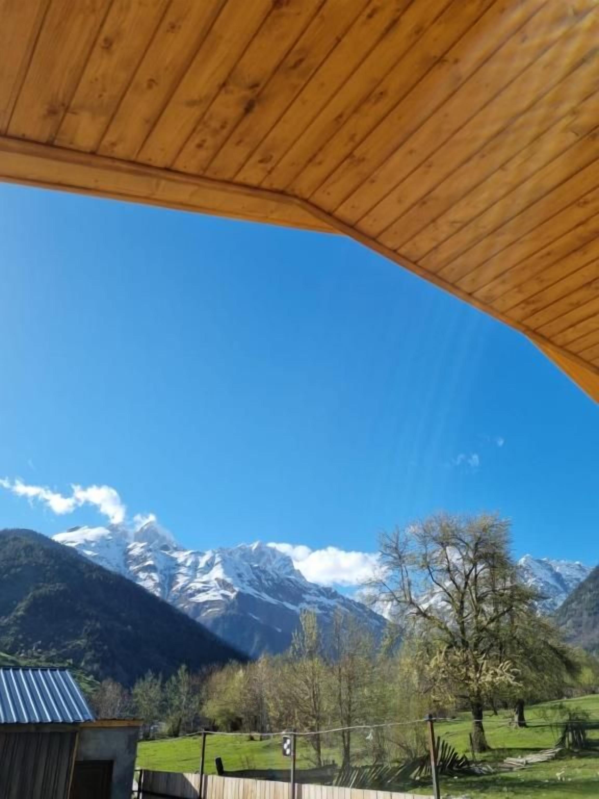 Een houten constructie met uitzicht op besneeuwde bergen en een helderblauwe lucht.