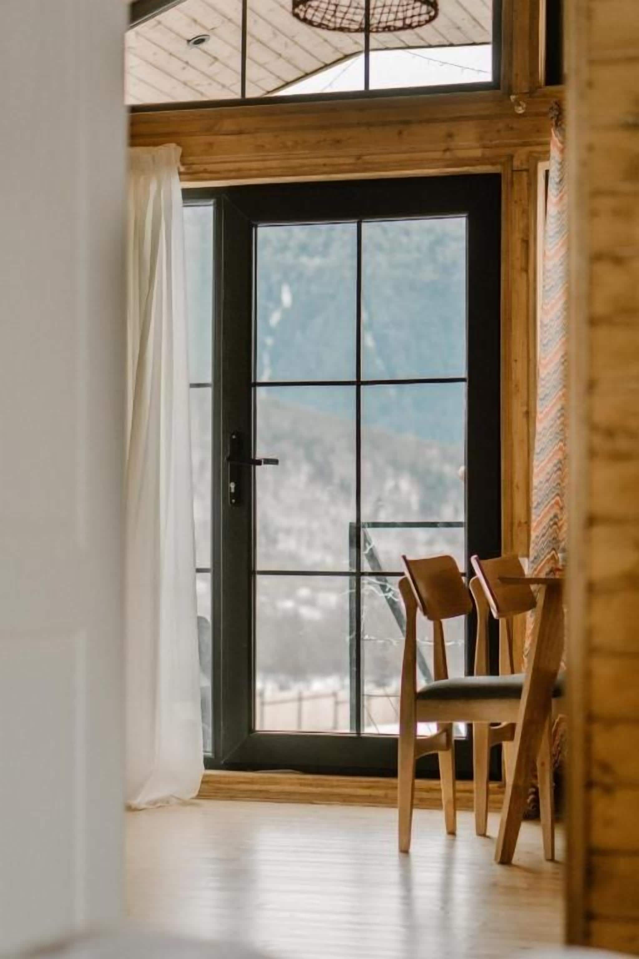 Una habitación con un ventanal grande, piso de madera y dos sillas de madera.