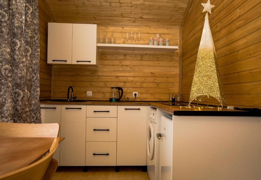 Una cocina compacta con paredes de madera, armarios blancos, una lavadora y un árbol decorativo navideño.