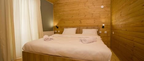 Een slaapkamer met houten lambrisering, een bed, twee nachtkastjes en een wandlamp.