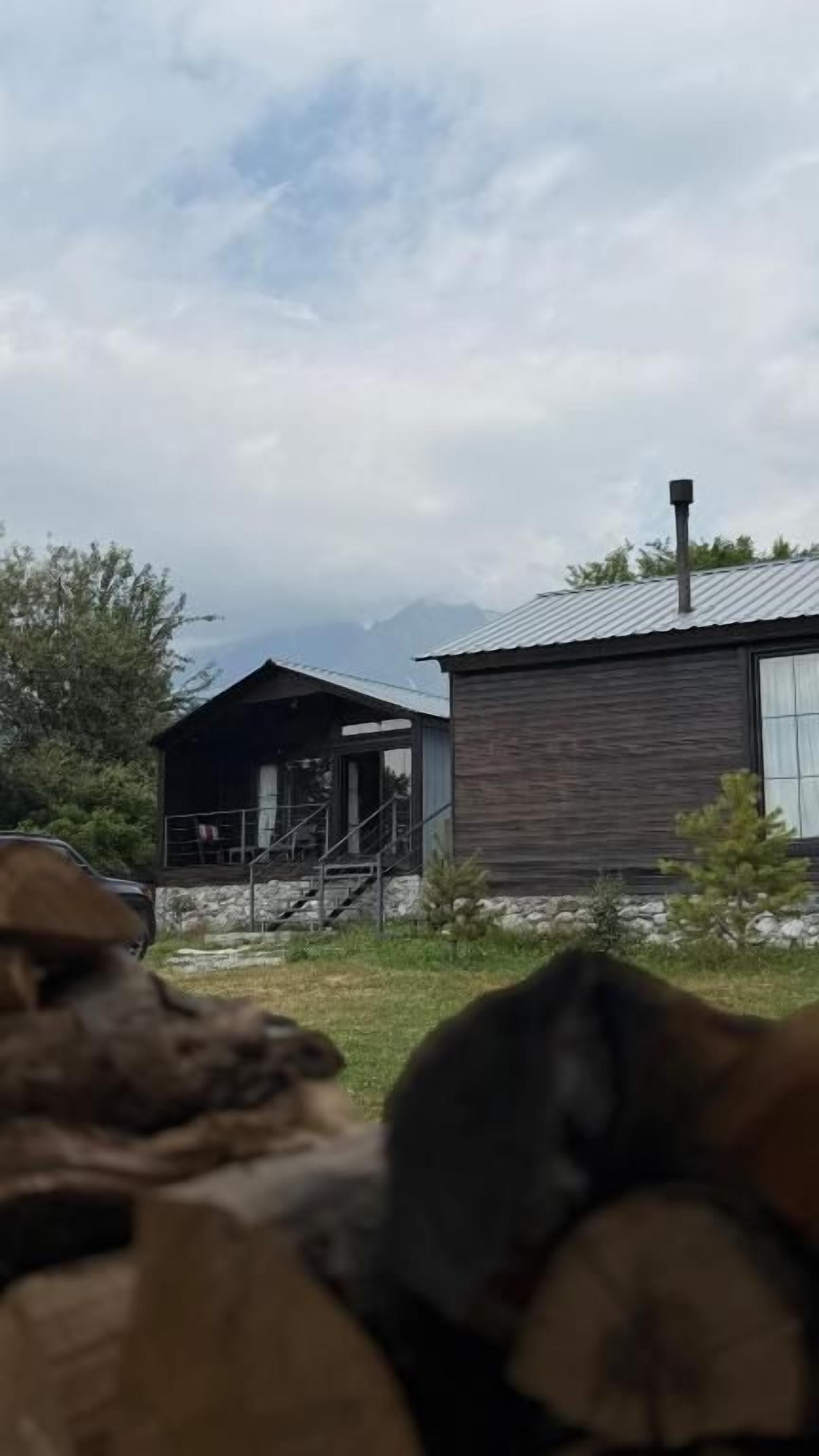 Een rustieke hut met een houten gevel, een schoorsteen en een klein terras.