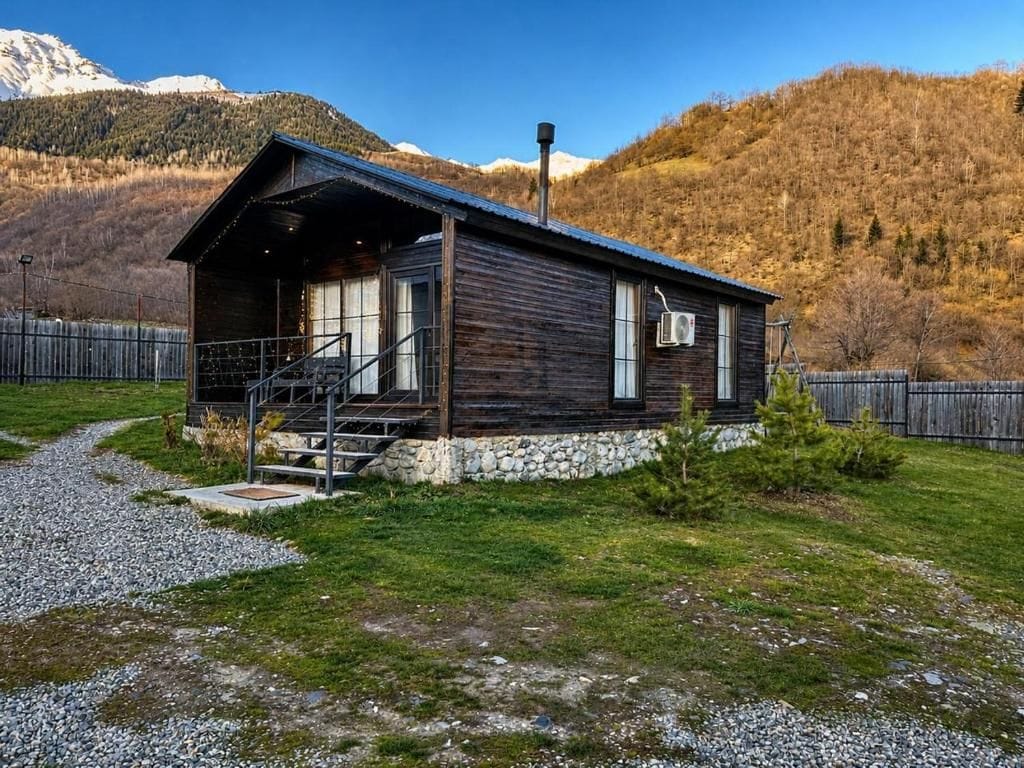 Une cabane en bois avec des fondations en pierre, une véranda et une vue sur une chaîne de montagnes boisée.