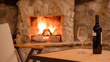 A stone fireplace with a fire, a bottle of wine, and a glass on a wooden table.