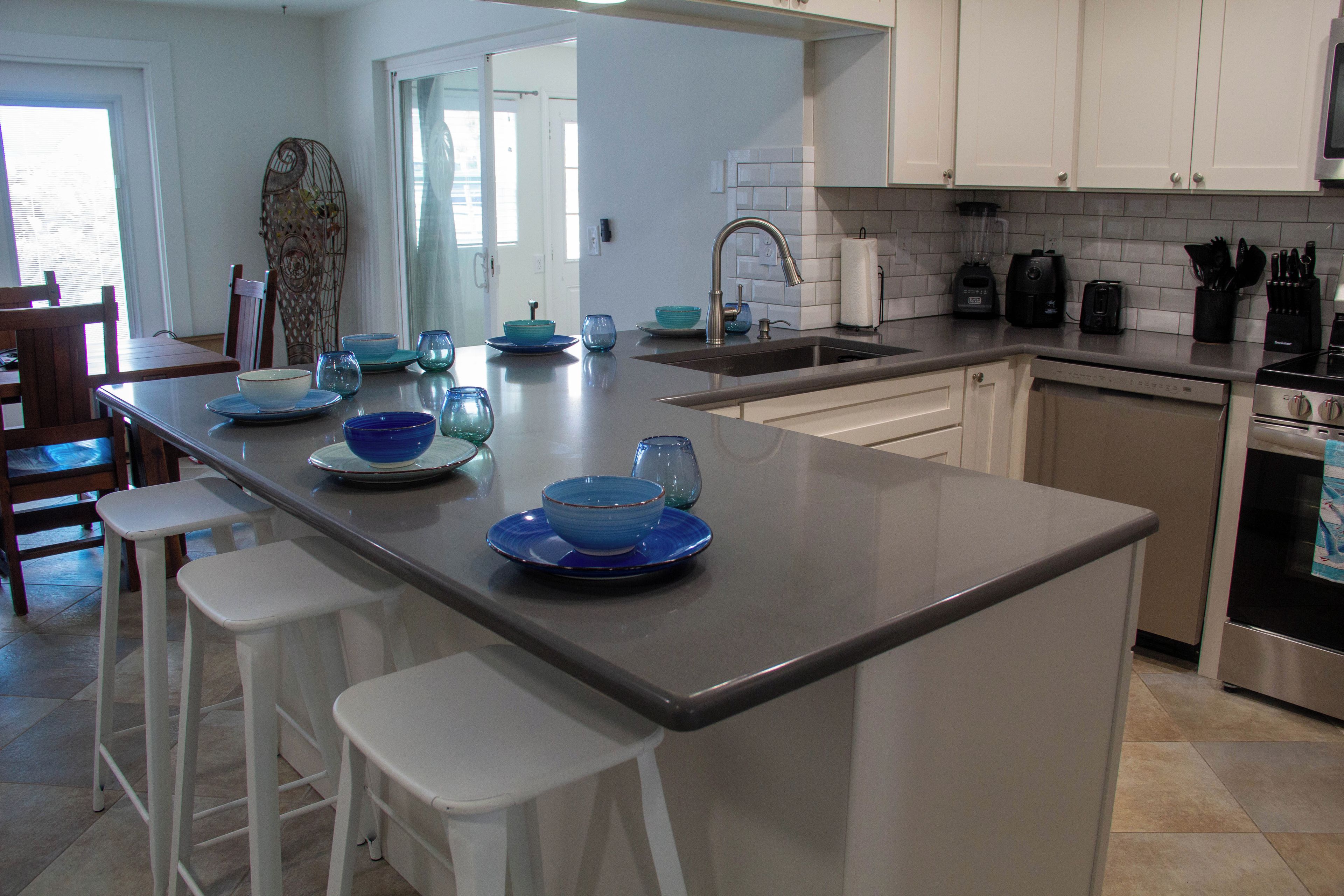 A modern kitchen with a central island, bar stools, a sink, and a stove.