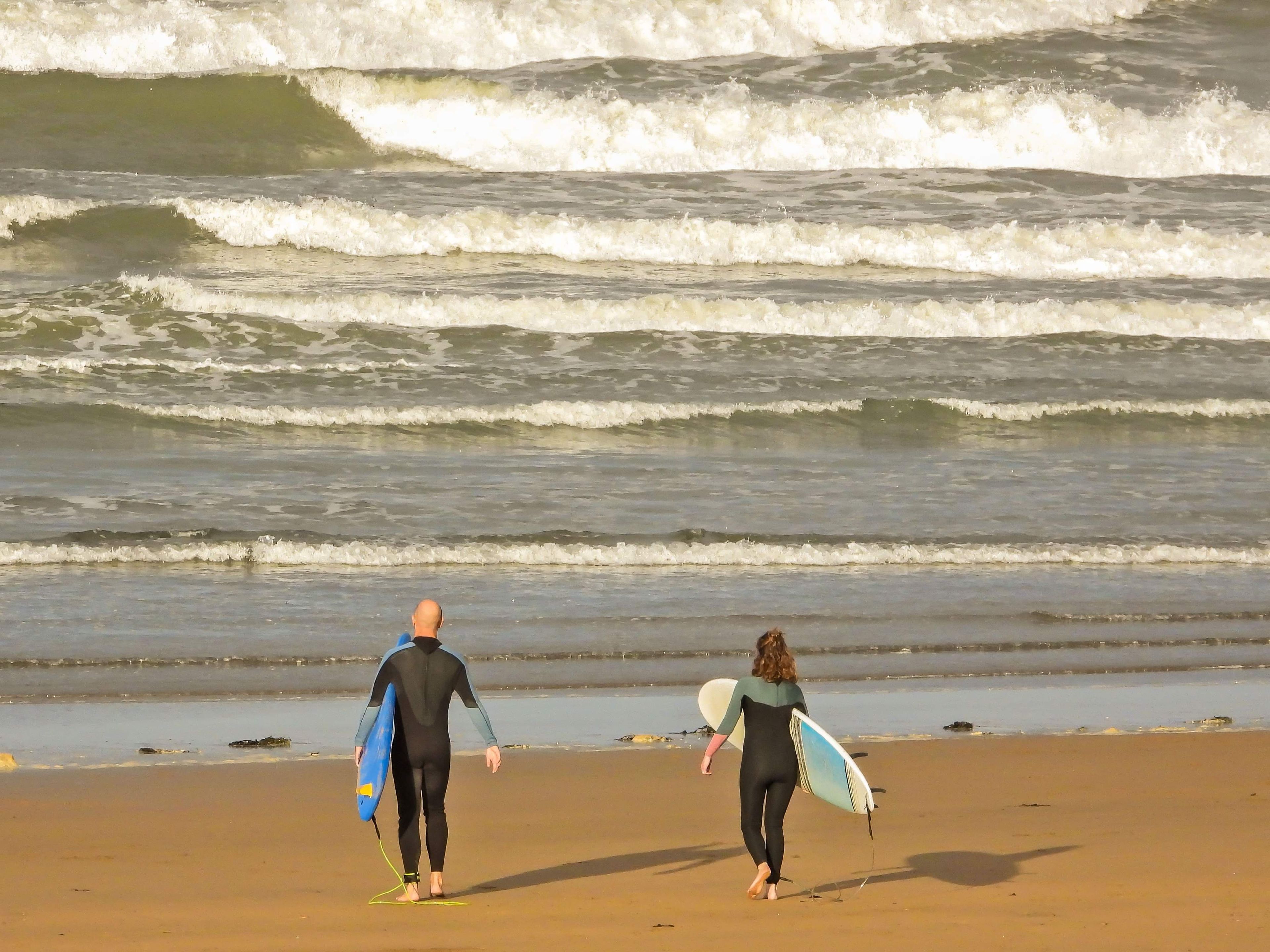 Two individuals walking on a sandy beach with waves in the background.