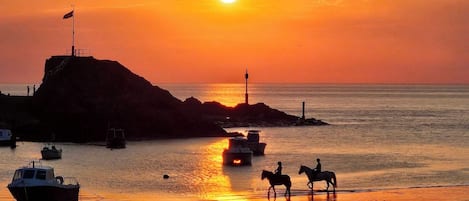 A sunset over a body of water with boats and a lighthouse.
