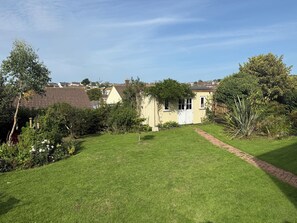 A well-maintained garden with a lawn, a pathway, and a small building with a door and windows. - Family home in Bude 5 minutes from beach – garden, private parking & storage. (Bude)