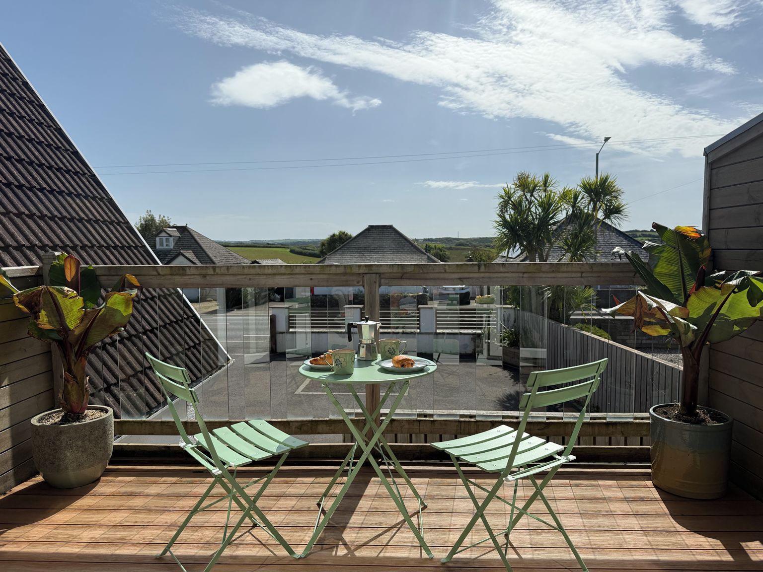 Ein Balkon mit Tisch und Stühlen, mit Blick auf eine Wohngegend mit Häusern und blauem Himmel.