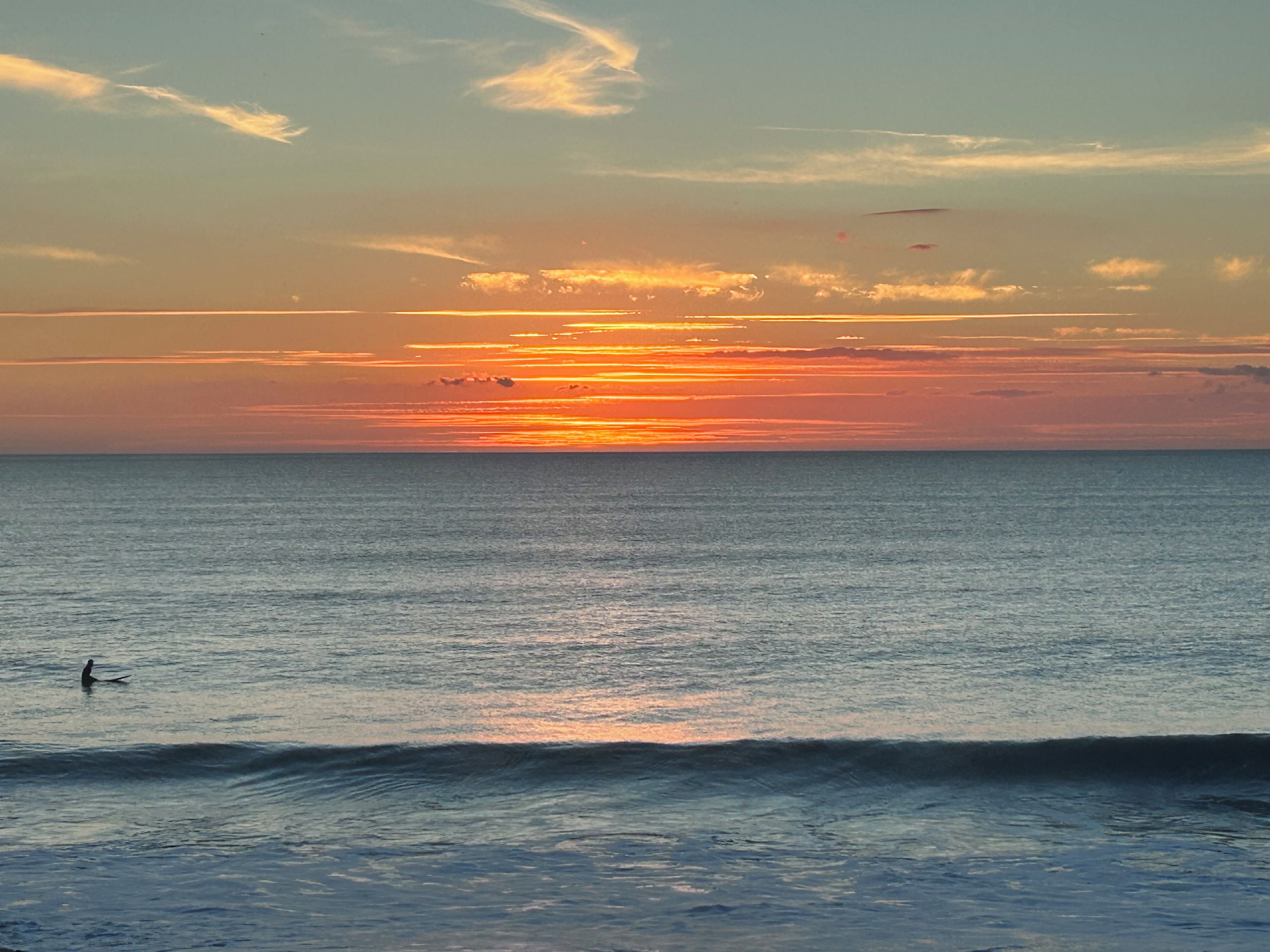 A sunset over the ocean with a person surfing.
