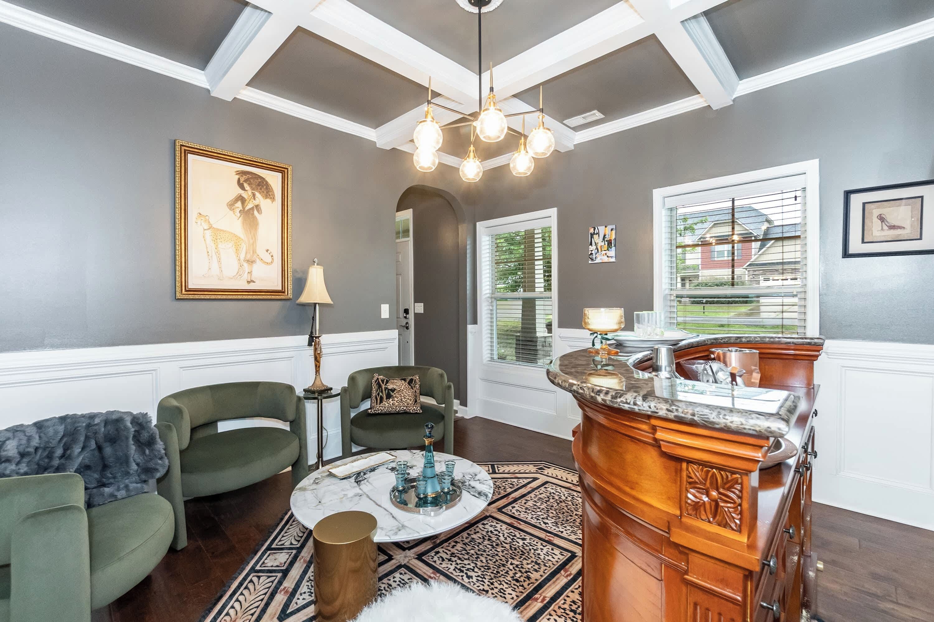 Un salon avec un plafond haut, un lustre, une cheminée et une vue sur l’extérieur.