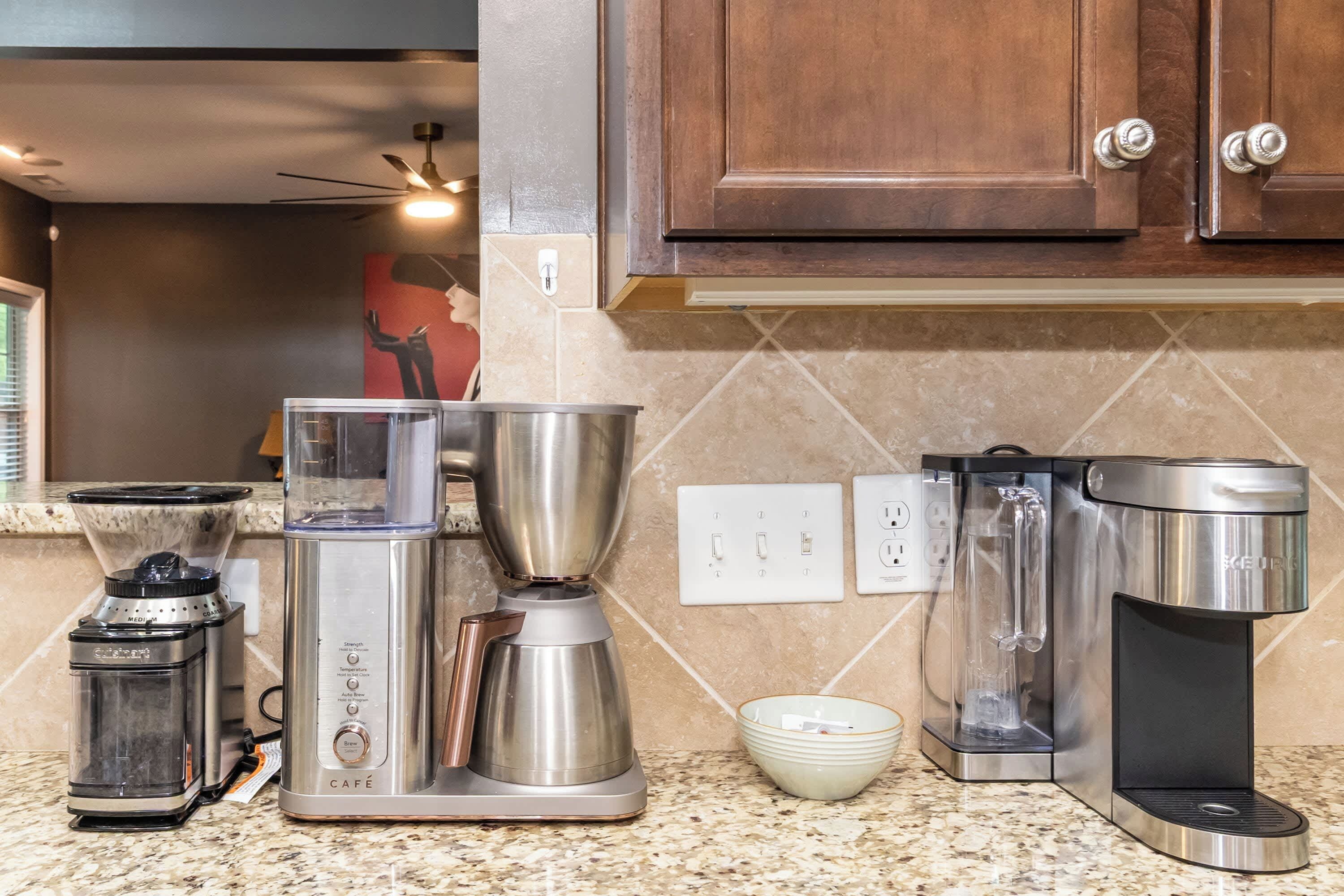 A kitchen with a coffee maker, grinder, and a kettle.