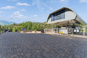 A paved area with a modern building, a sign with a mountain and a flag, and a warning sign. - Luxury Condo w/ Resort Amenities, Walk to Gondola (Avon)