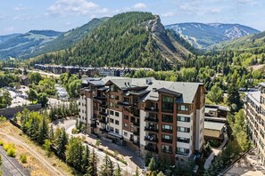 Ett hotell med flera våningar och balkonger, omgivet av skogbeklädda kullar och berg.