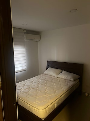 A bedroom with a bed, a window with blinds, and an air conditioning unit on the wall. - Quiet Apartment (Bucaramanga)