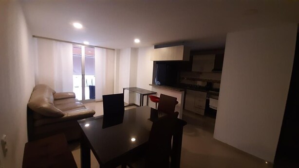 A modern living room with a sofa, a dining table, and a kitchen area with cabinets and a microwave. - Quiet Apartment (Bucaramanga)