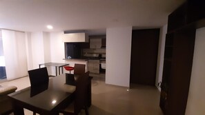 A modern kitchen with white cabinets, a dining area with a glass table, and a hallway leading to a door. - Quiet Apartment (Bucaramanga)