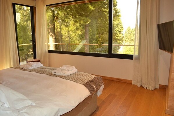 A bedroom with a large window, a bed, and a wooden floor.