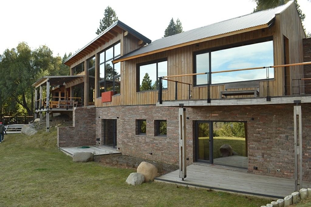 A modern two-story house with large windows, a wooden deck, and a stone foundation.