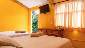 Ett hotellrum med två sängar, en byrå i trä, en platt-TV och ett fönster med gardiner.