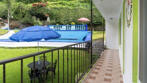A balcony with a view of a swimming pool, a blue umbrella, and a red umbrella.