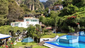 Ett semesterparadis med en swimmingpool, frodig grönska och en imponerande bergskedja i bakgrunden.