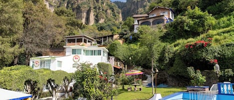 A resort with a swimming pool, lush greenery, and mountainous backdrop.