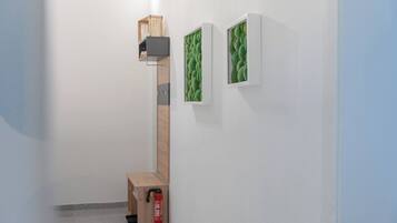 A hallway with a wooden ladder-like structure, a small table with a red object, and two framed pictures on the wall.