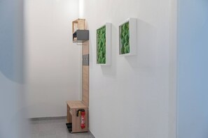 Un pasillo con una estructura de escalera de madera, una mesita con un objeto rojo y dos cuadros en la pared.