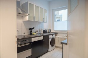 Eine kompakte Küche mit Backofen, Waschmaschine und einem Fenster mit Jalousien.