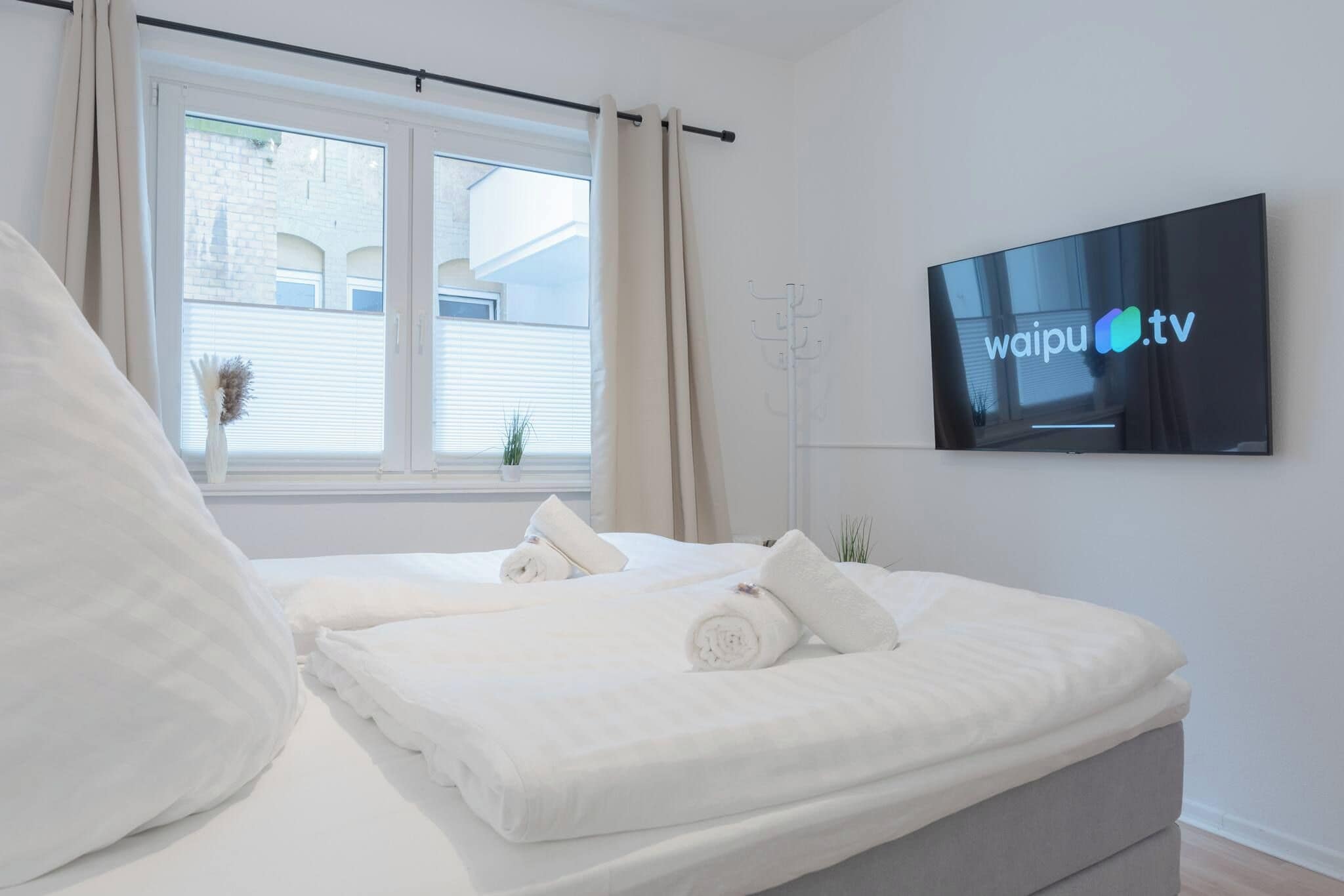 A modern bedroom with a bed, a TV mounted on the wall, and a window with curtains.