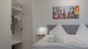 A hotel room with a bed, a painting of a cityscape, a bedside table with a lamp, and an open wardrobe. - Stylish and Central apt 4 Guests 56sqm top Location (Hannover)
