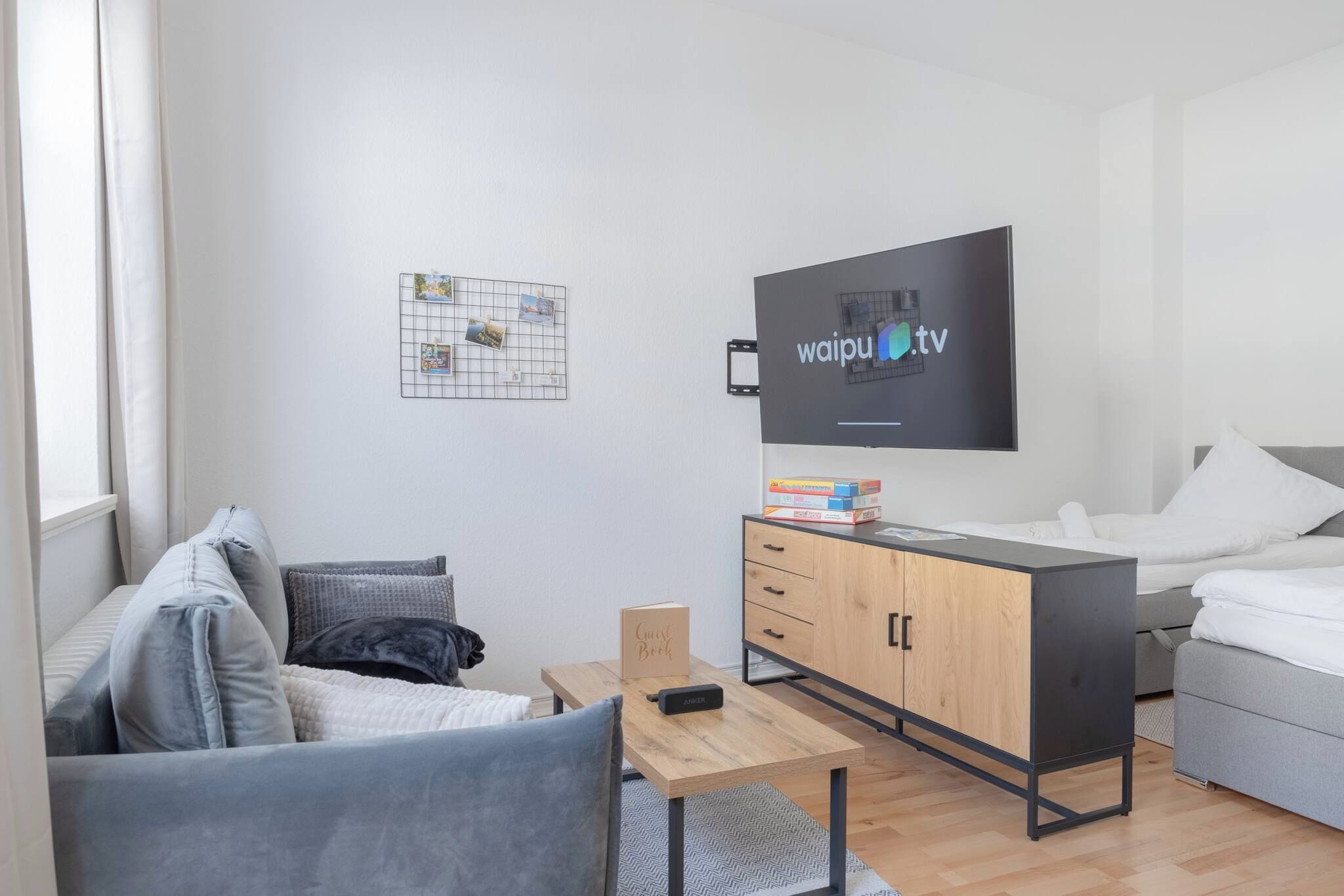 Una habitación de hotel moderna y bien iluminada, con una televisión de pantalla plana, un armario de madera, una mesita, un sofá y una cama.
