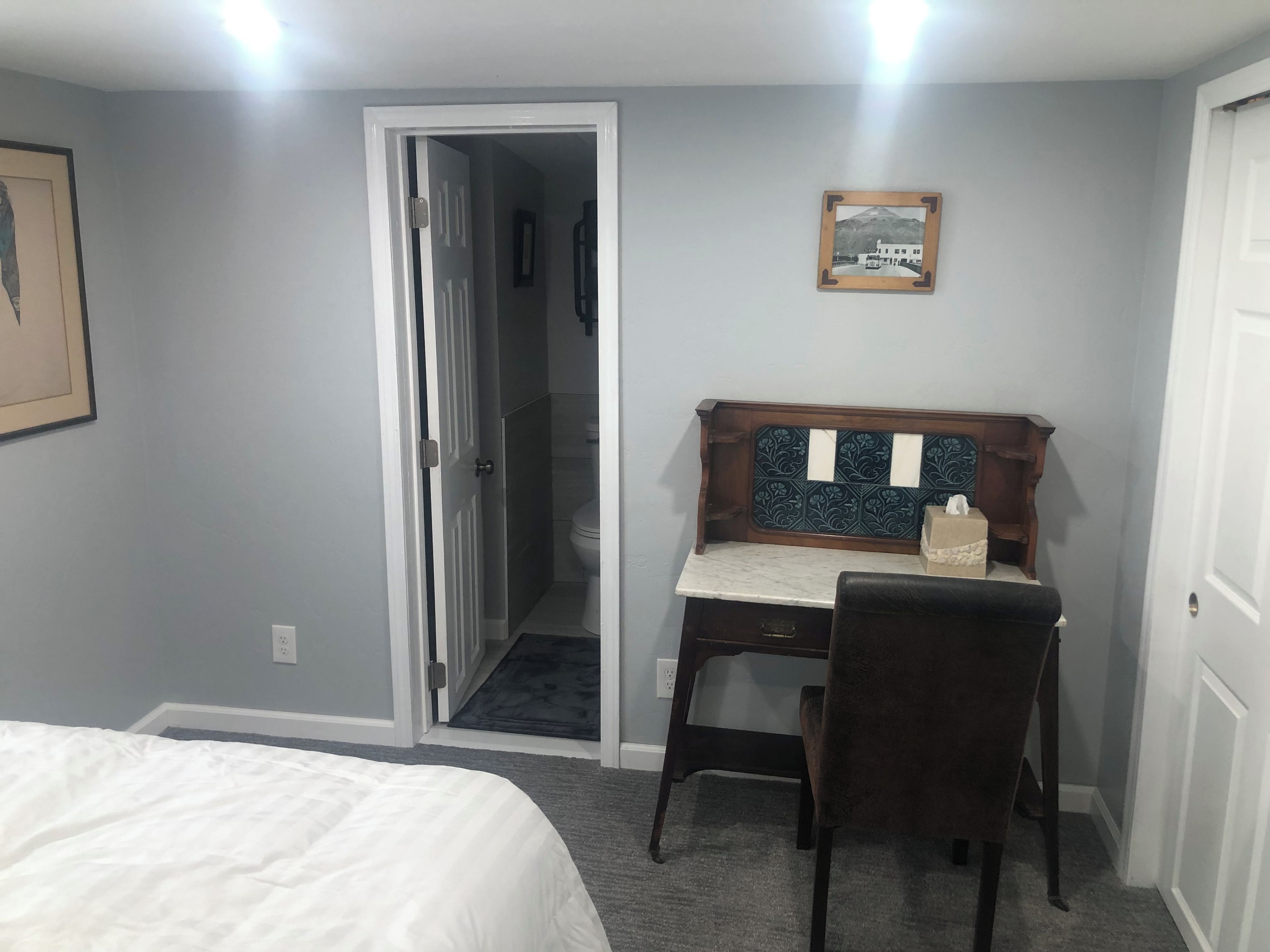 Une chambre à coucher avec un lit, un bureau et une chaise. Une porte donne accès à une salle de bain.