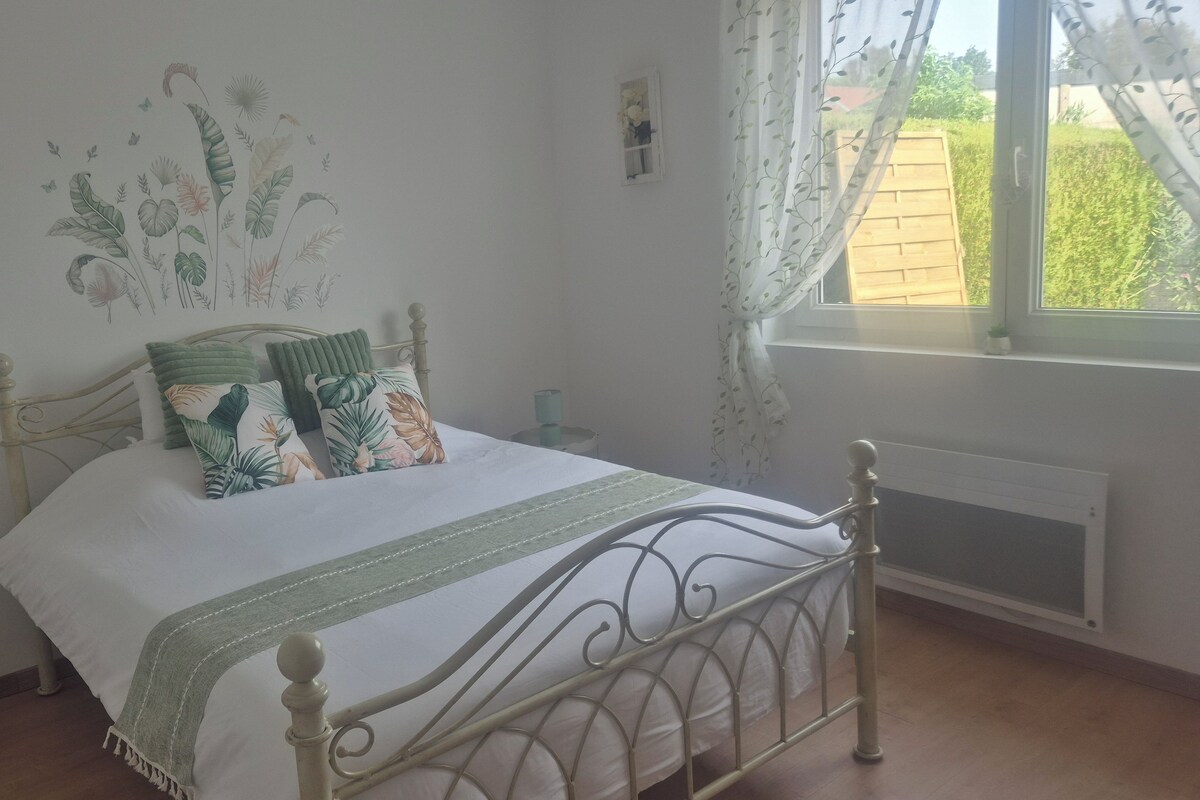Une chambre à coucher comprenant un lit, une table de chevet, une fenêtre avec des rideaux et un mur orné d’une fresque à motifs végétaux.
