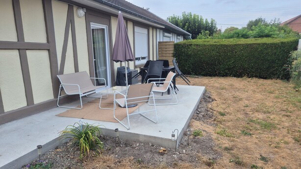 A patio with outdoor furniture, a grill, and a hedge.