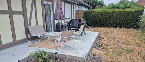A patio with outdoor furniture, a grill, and a hedge.