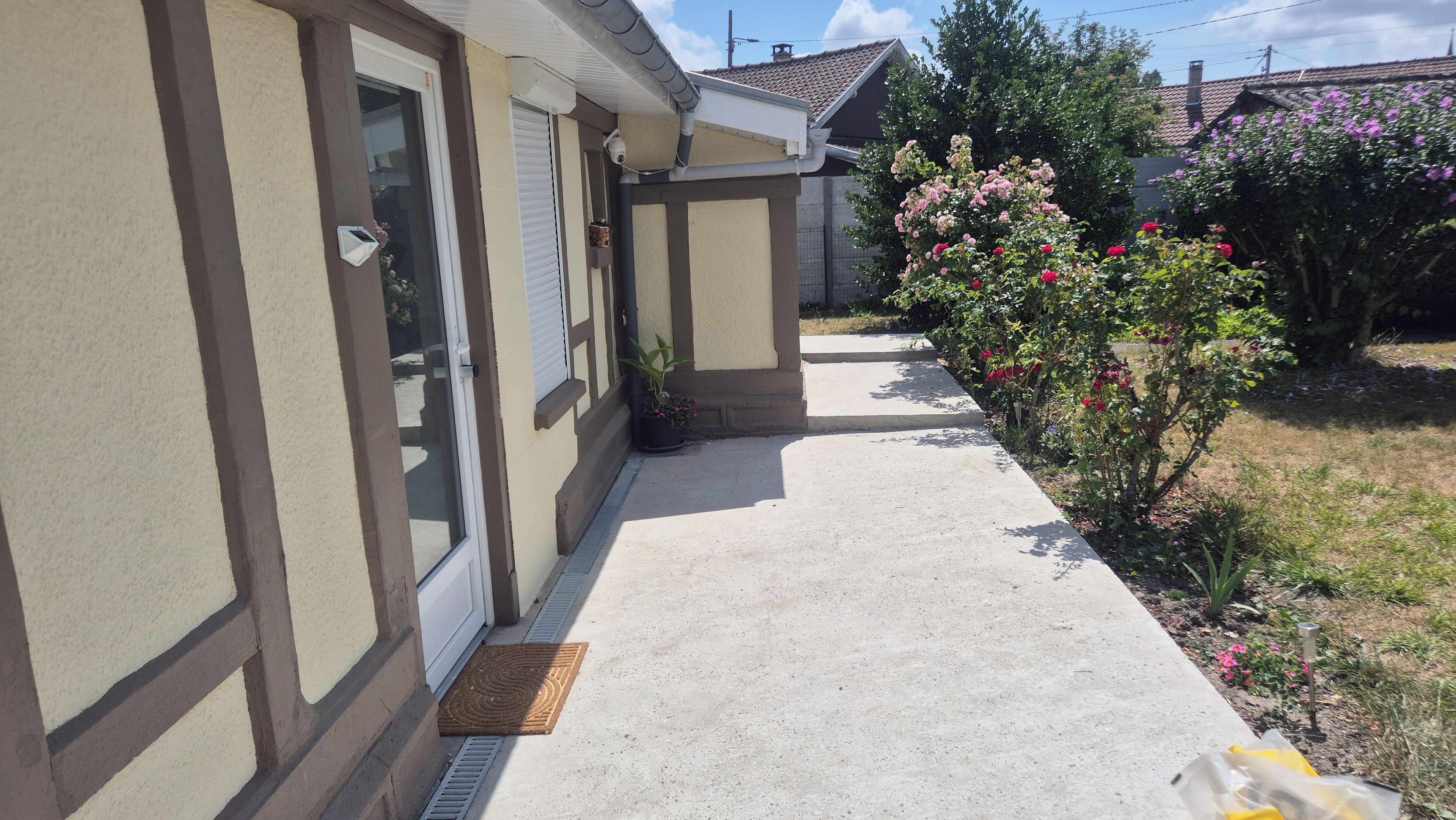 Een woonhuis met een oprit van beton, een deur met raam en een tuin met bloeiende planten.