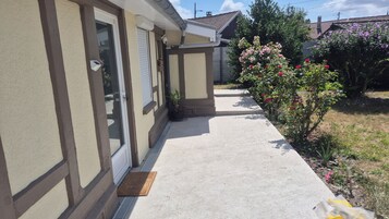 Una casa residencial con un camino de hormigón, una puerta con ventana y un jardín con plantas en flor.