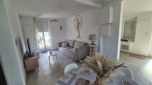 Un salon avec un canapé, une table basse et une lampe. Une porte donne accès à un balcon.