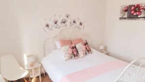 A bedroom with a metal bed frame, a bedside table, a chair, and a wall-mounted lamp.