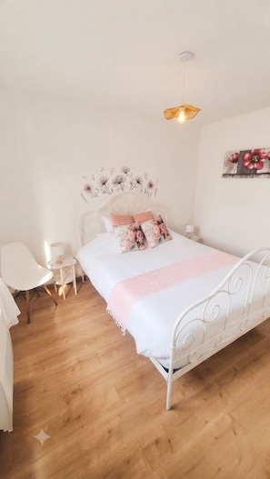 Un dormitorio con una cama de metal blanco, una mesita de noche, una silla y una lámpara colgante.