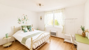 A bedroom with a bed, bedside tables, a radiator, a window with curtains, a chair, and a small table with a plant.
