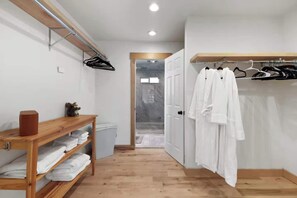 A hallway with a wooden bench, a coat rack with white robes, and a door leading to another room.