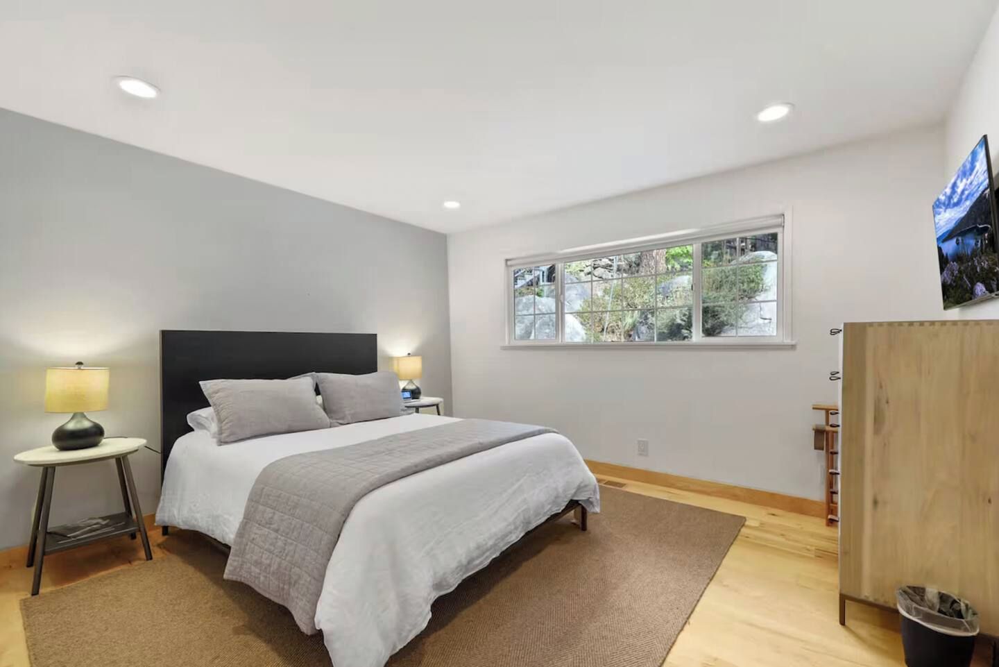 A bedroom with a bed, bedside tables, a window with a view, and a wooden wardrobe.
