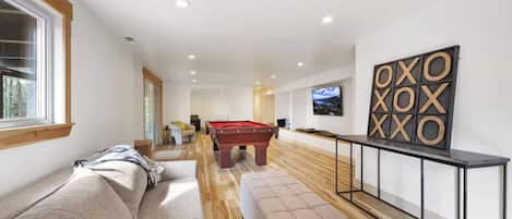 A modern living room with a pool table, a sofa, and a television.