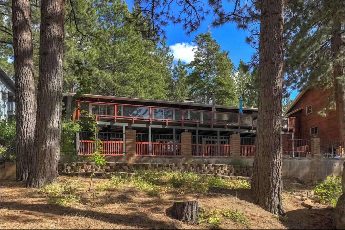 Back view of the home surrounded by tall pines, showing the expansive decks and peaceful forest setting.